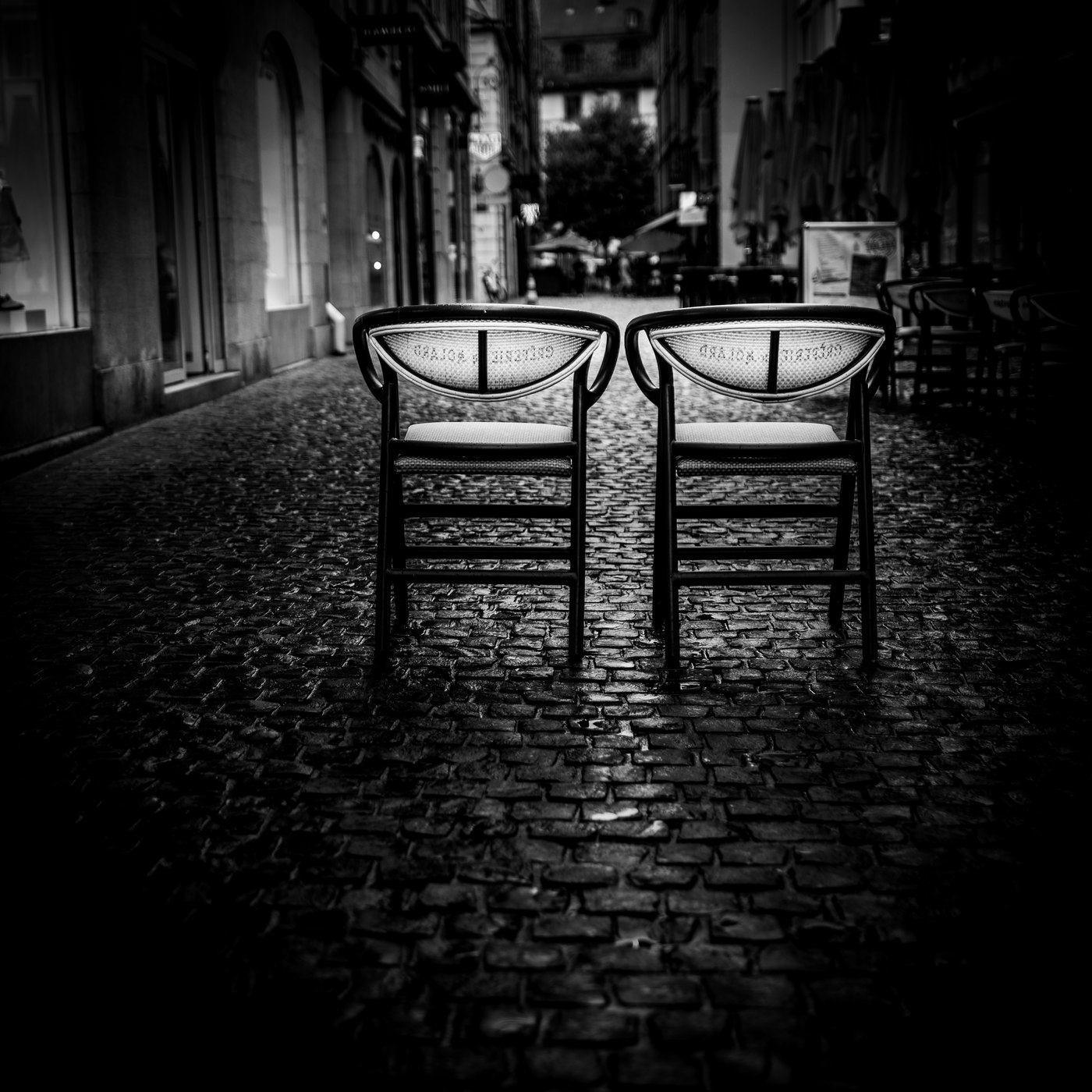 Deux chaises identiques, dossiers face à face, dans une ruelle pavée le soir