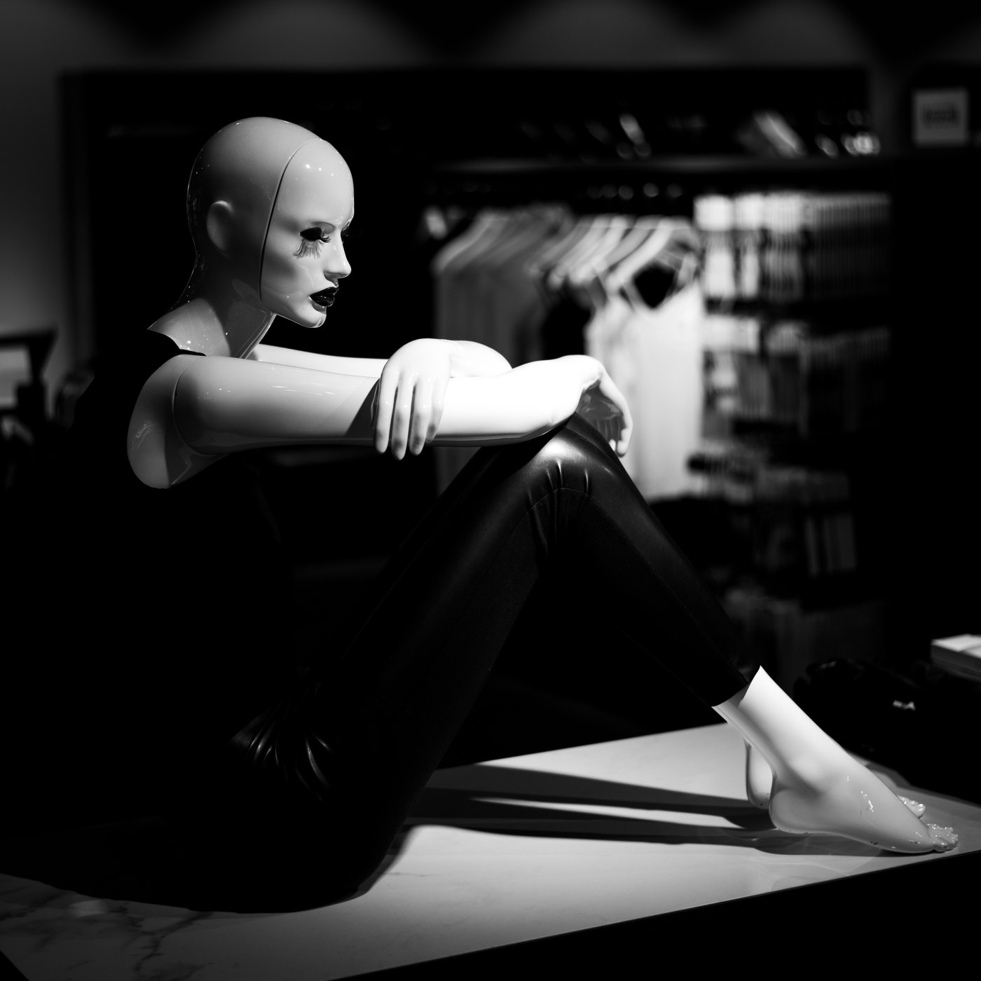 Mannequin assis en vitrine, genoux repliés, bras posé sur le genou