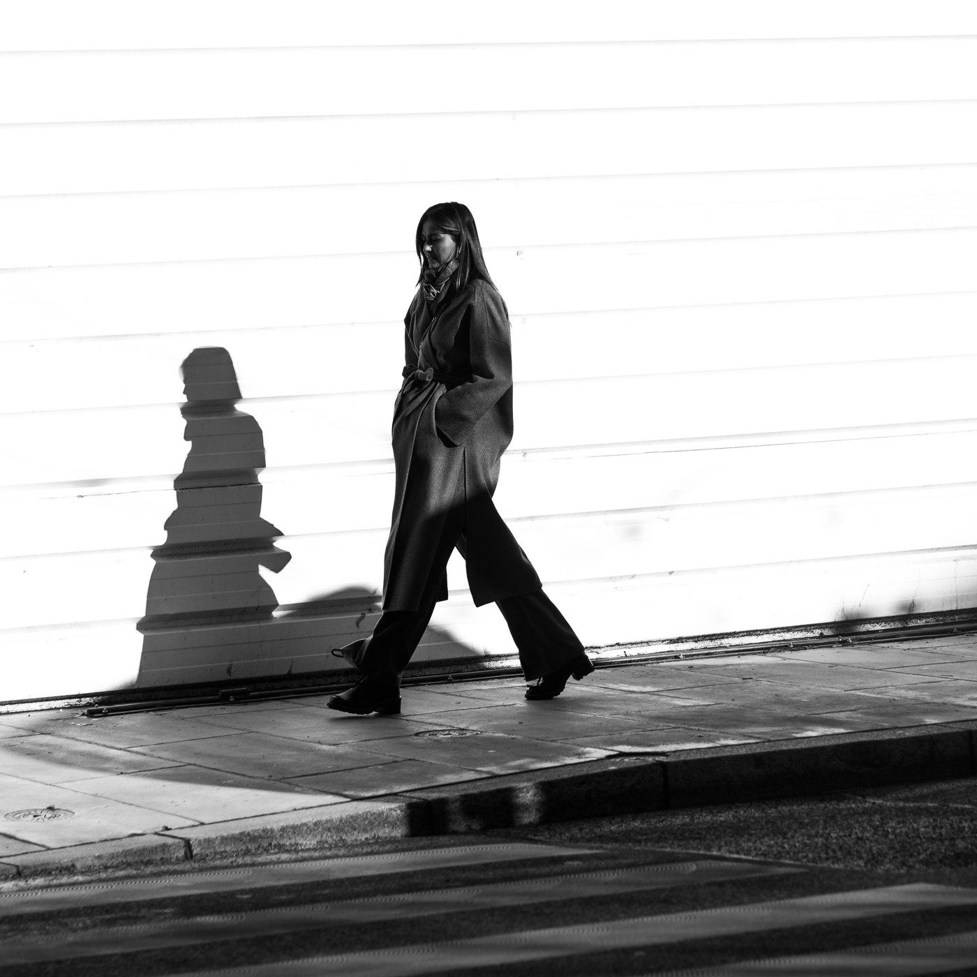 Une femme marche, son ombre projetée sur un mur clair derrière elle