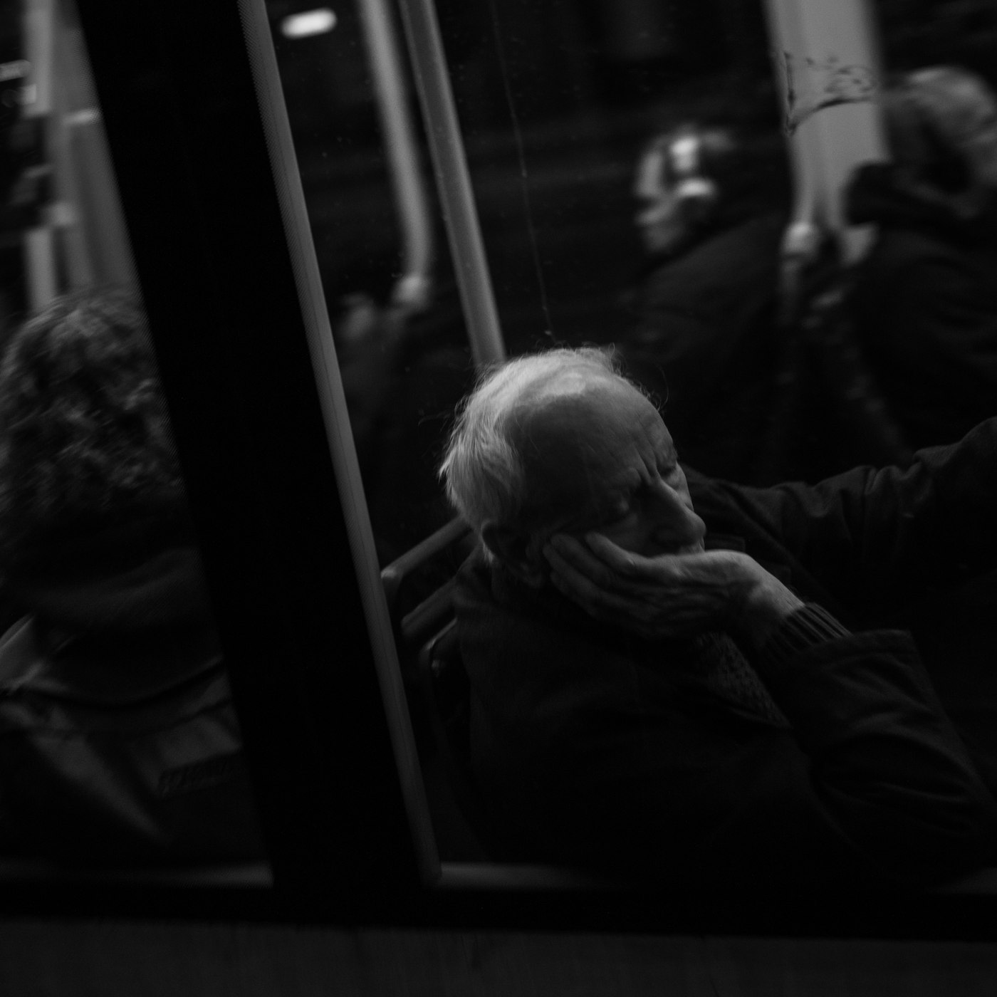 Un homme âgé, assis dans un tram la nuit, le visage dans la main
